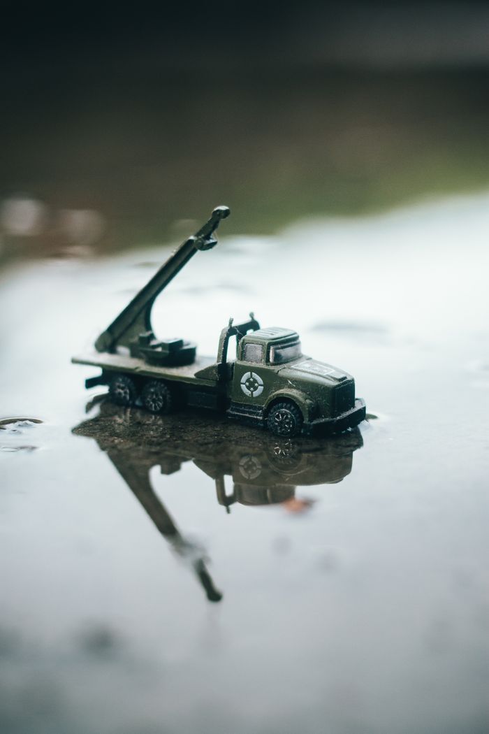 Detailed shot of a small green military toy truck reflected in water, creating a dramatic scene.